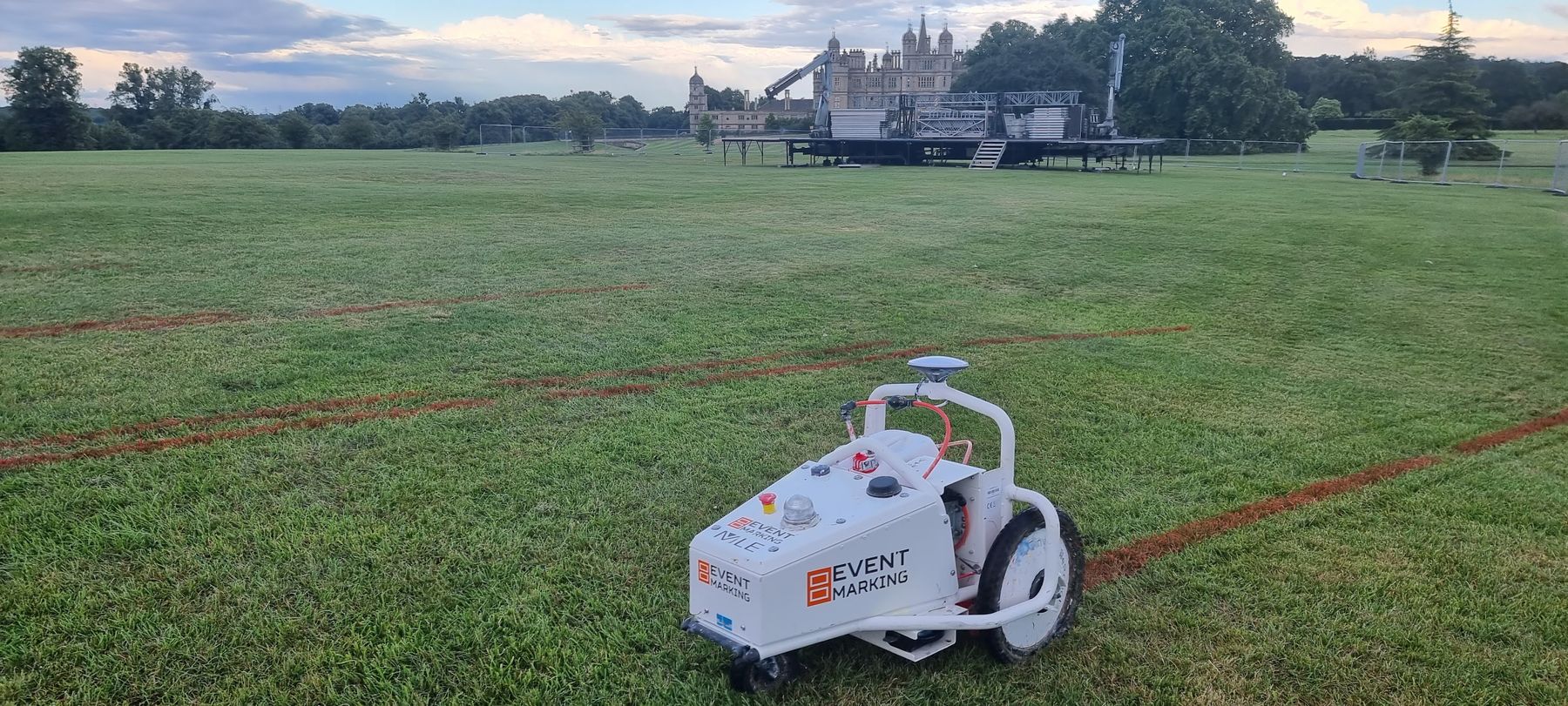 Event Marking GPS robot on a field with red layout markings, a stage and Burghley House behind it