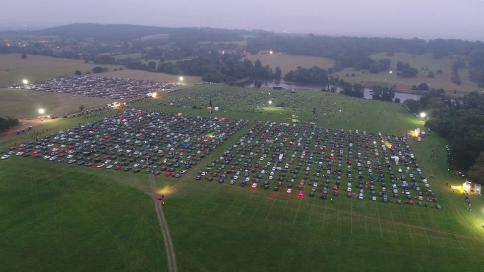 Aerial view at dusk of an outdoor event with cars arranged in rows on marked grass fields