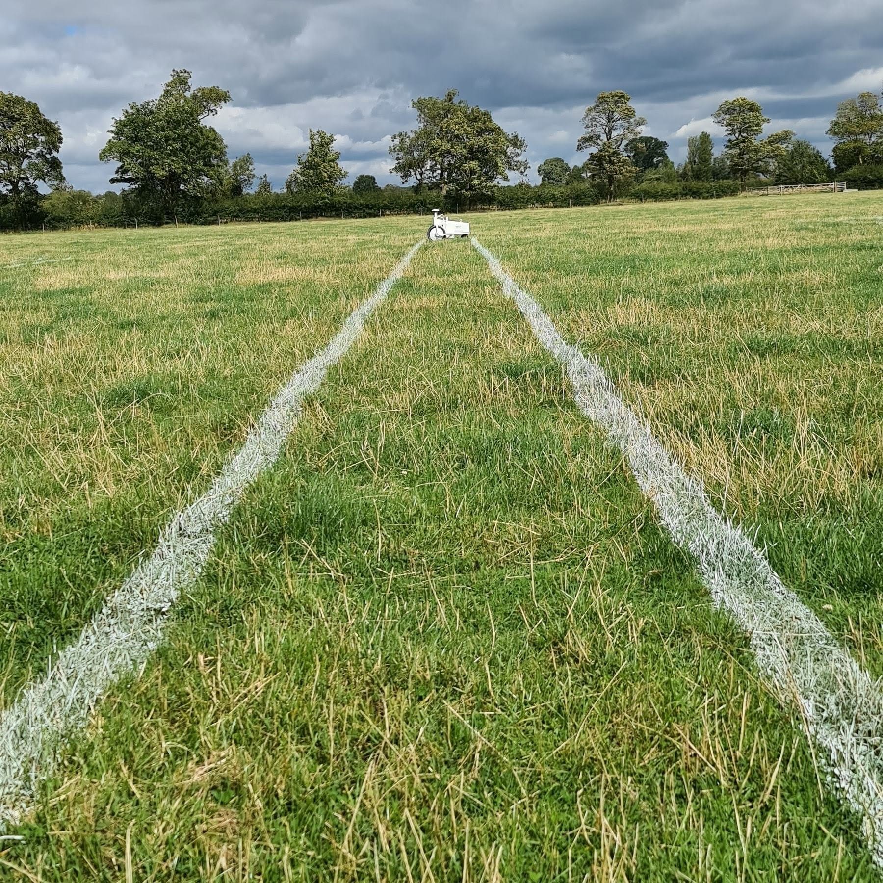 A GPS line marking robot ahead of two straight white lines painted across a grass field