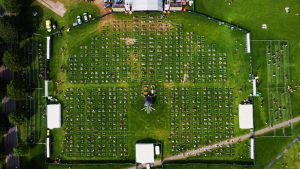 Aerial view of an outdoor concert with socially distanced seating sections arranged in a grid on a large grassy area, featuring precise event site marking.