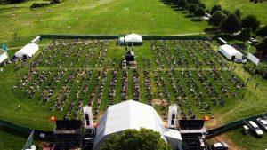 Aerial view of an outdoor event site marking with spaced seating, a stage, and surrounding greenery on a sunny day.